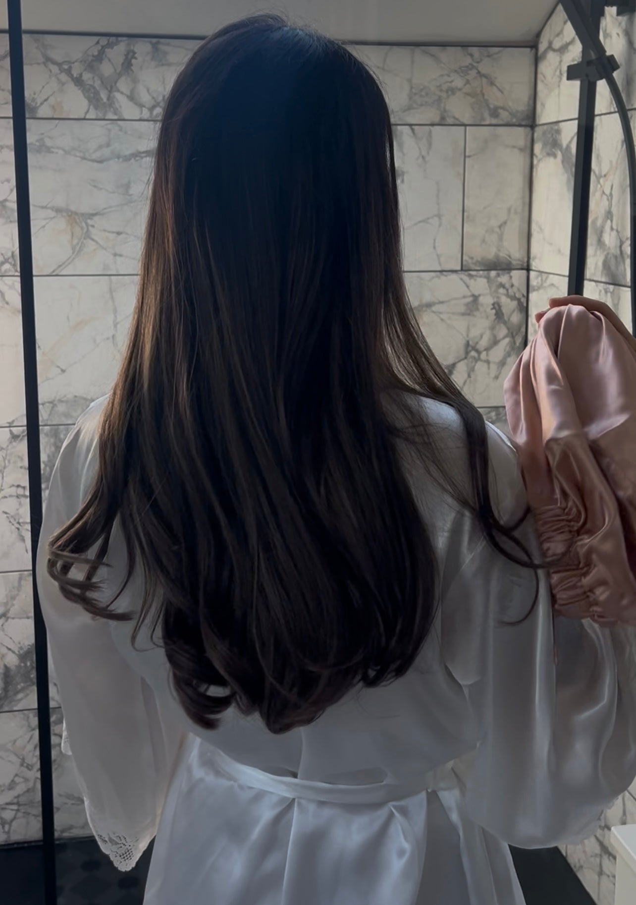 Model with healthy, voluminous hair holding the Haus Gio silk bonnet in her hand, highlighting the bonnet’s smooth, luxurious texture and elegant design.